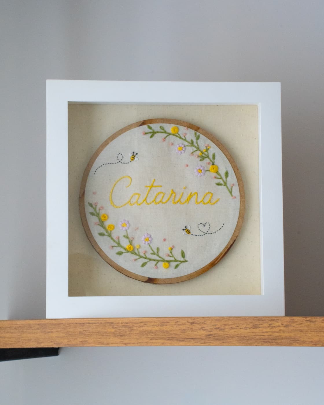 Quadro branco com bastidor bordado: o nome Catarina entre flores e abelhas